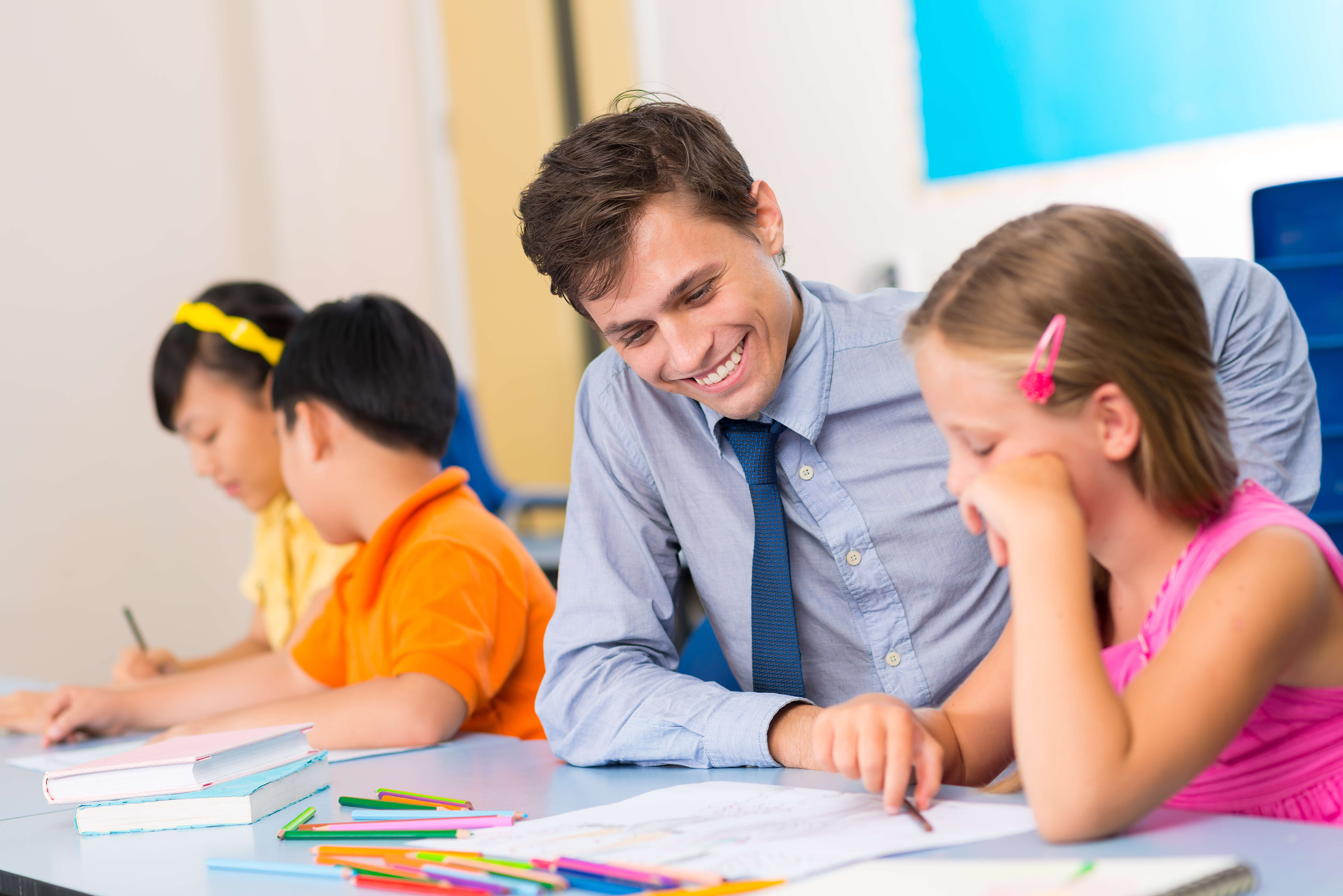 male ECT sat at a desk with students helping them with their work